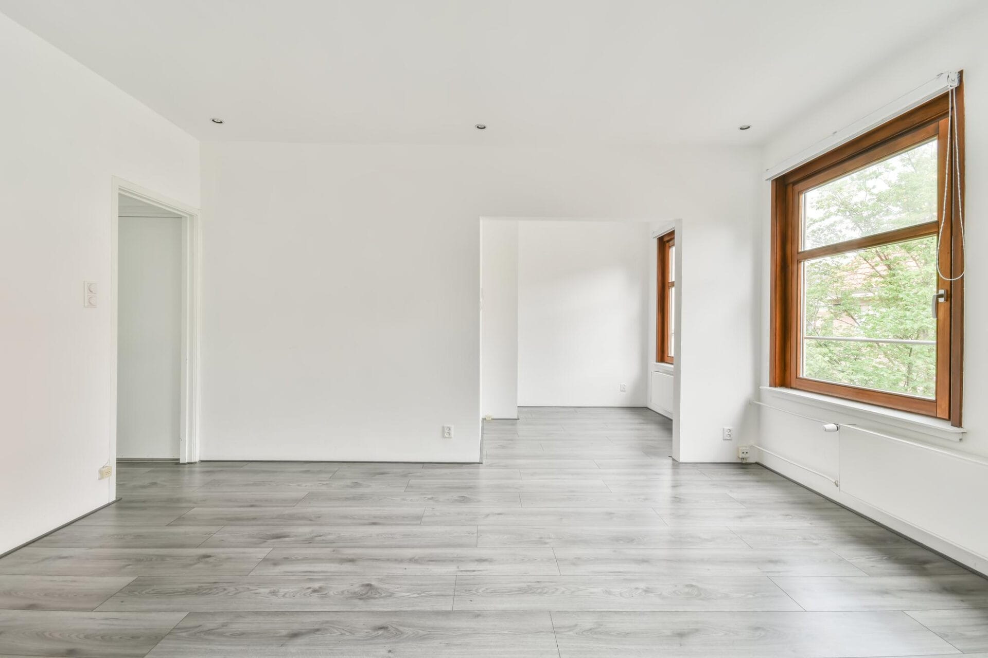 Bright, empty room with large windows, white walls, and gray wood flooring—fresh and spotless after thorough builder cleaning following recent renovation work.